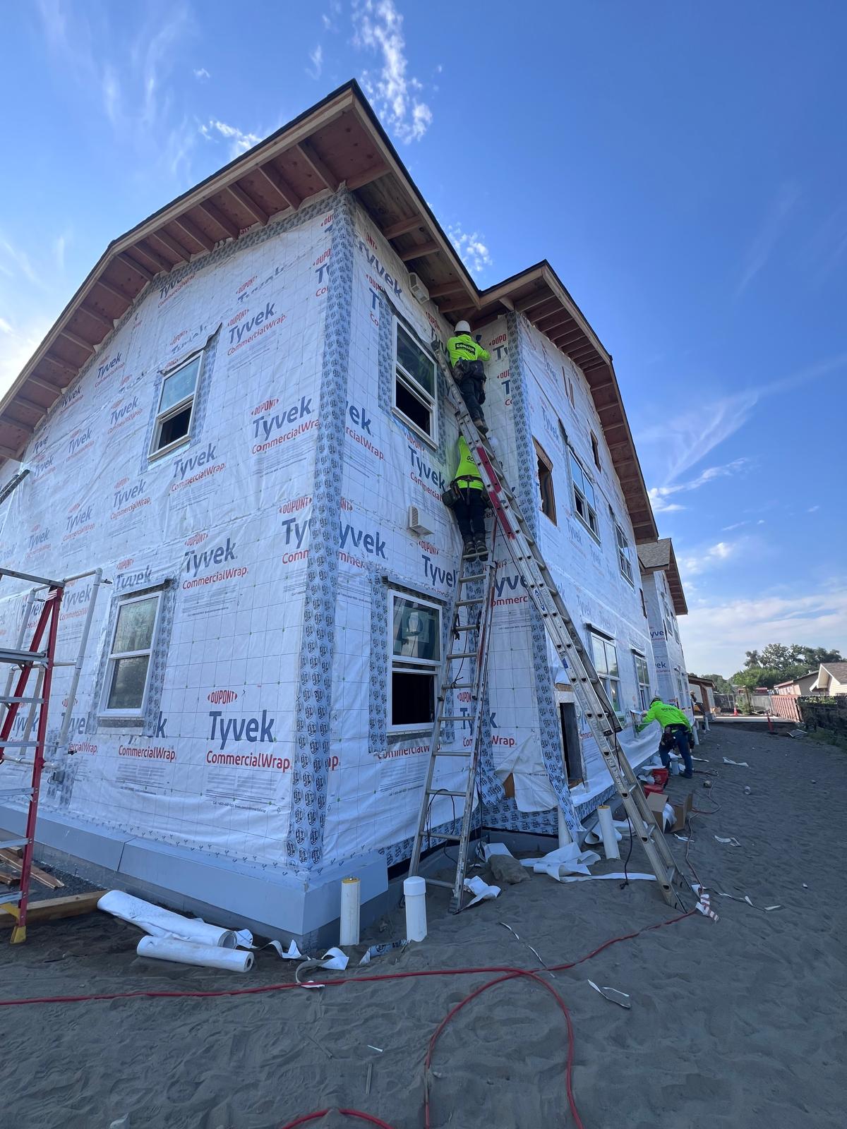 Crew on ladders installing WRB and windows on the corner elevation